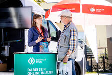 Die Mobilreferentin steht am Stand vor dem Infomobil und ber&auml;t einen Besucher.