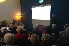 Eine Seniorengruppe sitzt im Saal und h&ouml;rt dem Vortrag des digitalen Engels zu zu