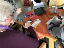 &auml;ltere Frau am sitzt am Tisch und bedient ihr Smartphone