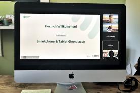 Computer Monitor mit dem Bild einer Videokonferenz in der eine Pr&auml;sentation zum Thema Smartphone & Tablet Grundlagen zu sehen ist