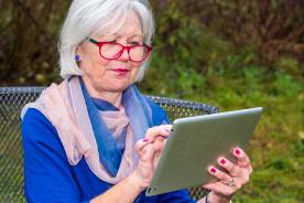 Seniorin sitzt auf der Bank und h&auml;lt Tablet in der Hand