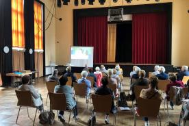 Senioren sitzen im Saal und h&ouml;ren einer Pr&auml;sentation zu