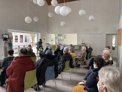 Die Teilnehmenden sitzen im Raum und schauen zur Pr&auml;sentation nach vorne auf einen gro&szlig;en Flachbildschirm