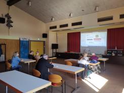 Die Teilnehmenden sitzen im Raum und schauen zur Pr&auml;sentation an der Wand