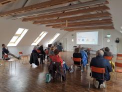 Die Teilnehmenden sitzen im Raum und schauen zur Pr&auml;sentation an der Wand