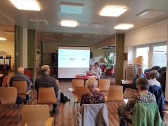 Die Teilnehmenden sitzen im Raum und schauen zur Pr&auml;sentation an der Leinwand