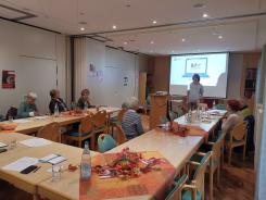 Die Teilnehmenden sitzen im Raum und blicken zu unserem Referenten und zur Pr&auml;sentation an der Wand