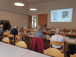 Die Teilnehmenden sitzen im Raum und schauen zur Pr&auml;sentation an der Wand