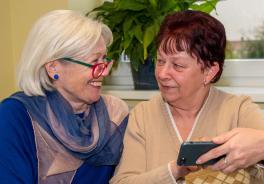 zwei Frauen schauen auf ein Smartphone und l&auml;cheln