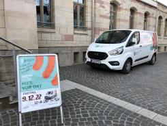 Das Engel-Mobil steht vor dem Bahnhofsgeb&auml;ude. Im Vordergrund steht ein Aufsteller mit der Information, dass am 09.12.2022 hier der Digitale Engel zu Besuch ist.