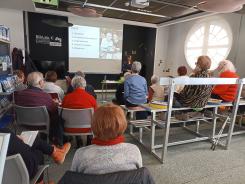 Senior:innen sitzen auf St&uuml;hlen und B&auml;nken (von hinten fotografiert). Der Blick richtet sich nach vorne auf die Referentin vom Digitalen Engel mit einer Pr&auml;sentation.