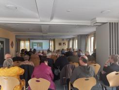 Die Teilnehmenden sitzen im Raum und schauen zur Pr&auml;sentation an der Leinwand