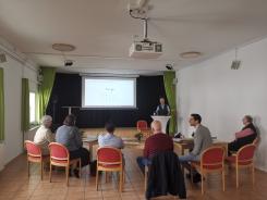 Die Teilnehmenden sitzen im Raum und blicken zur Pr&auml;sentation an der Wand