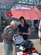 Petra zeigt einer Seniorin drau&szlig;en am Infostand Dinge am Smartphone.
