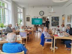 Die Teilnehmenden sitzen im Raum und schauen zur Pr&auml;sentation auf dem Bildschirm 
