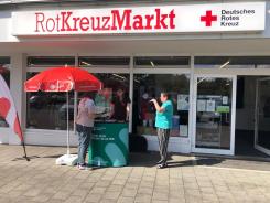 Petra steht gemeinsam mit einer Dame am Info-Stand vor dem RotKreuzMarkt. Eine weitere Dame l&auml;uft zum Stand.