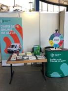 Der Info-Stand mit Roll Up, Tisch und Materialien sowie das Gl&uuml;cksrad auf dem Messetresen.