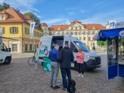 Ein Besucher steht vor dem Infomobil an einem Stehtisch und unterh&auml;lt sich mit einem Mitglied des Technikcafes Tettnang
