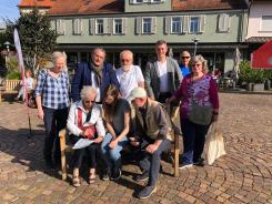 Petra sitzt mit einem &auml;lteren Ehepaar auf einer Bank. Hinter ihnen stehen Frau Enders (Seniorenbeirat), der Landrat Schellhaas, Erwin Scharth, B&uuml;rgermeister Haus und Herr Scharths Freundin.