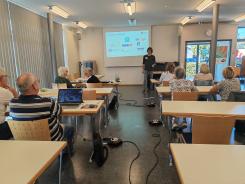 Die Teilnehmenden sitzen im Raum und schauen zur Pr&auml;sentation an der Leinwand