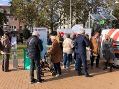 Zw&ouml;lf Personen stehen vor und neben dem Info-Stand mit dem Info-Mobil und unterhalten sich in verschiedenen Gruppen.