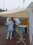 Petra steht mit einer Dame am Info-Stand. Der Info-Stand ist mit einem Pavillon vor dem Regen gesch&uuml;tzt.