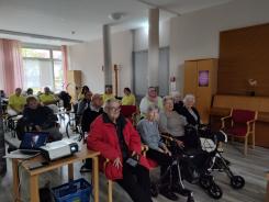 Die Teilnehmenden sitzen auf St&uuml;hlen im Raum und blicken zur Leinwand nach Vorne