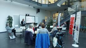 Theresa begr&uuml;&szlig;t die Teilnehmenden zu der Informationsveranstaltung in einer gr&ouml;&szlig;eren Glashalle.