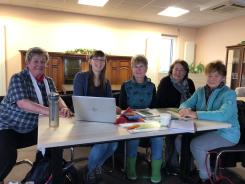 Petra sitzt mit vier Seniorinnen an einem Tisch auf dem ein Laptop steht. Alle f&uuml;nf Personen schauen und l&auml;cheln in die Kamera.