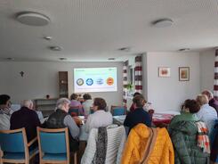 Die Teilnehmenden sitzen im Raum und schauen zur Pr&auml;sentation an der Leinwand