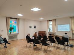 Die Teilnehmenden sitzen im Raum und schauen zur Pr&auml;sentation an der Leinwand