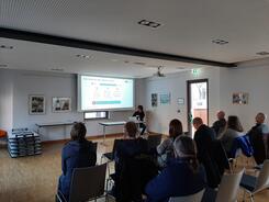 Die Teilnehmenden sitzen im Raum und schauen zur Pr&auml;sentation an der Leinwand