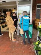 Theresa liest am Infostand zwei Besucherinnen eine Frage aus dem Digitalf&uuml;hrerschein vor. Sie stehen zusammen vor dem Supermarkt.