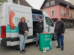 Johannes steht hinter dem Infostand vor dem Infomobil und neben ihm steht Frau Camus von der B&uuml;cherei, sowie ein Herr