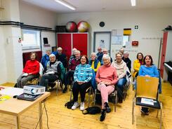 Rund 15 Senior:innen sitzen auf St&uuml;hlen in einem Raum des Kulturhofs und gucken nach vorne in die Kamera.