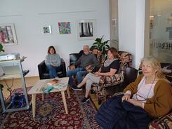 Zwei Teilnehmerinnen, ein Teilnehmer und Theresa sitzen im Ruheraum der Bibliothek auf Sesseln und l&auml;cheln in die Kamera.