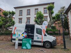 Das Infomobil steht mit Beachflag, Prospektst&auml;nder und Gl&uuml;cksrad vor einem Haus