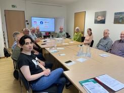 Die 11 Teilnehmenden aus Wunstorf sitzen an einem rechteckigen Gruppentisch und l&auml;cheln in die Kamera. Hinter ihnen ist die Endfolie der Pr&auml;sentation.
