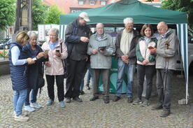 Theresa sowie 6 Besucher:innen und ein Ehrenamtlicher stehen vor einem gr&uuml;nen Pavillon und schauen zusammen auf die mitgebrachten Smartphones und Tablets.