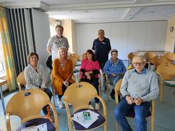 Auf dem Gruppenfoto sitzen f&uuml;nf Frauen und ein Mann auf St&uuml;hlen. Hinter ihnen stehen zwei M&auml;nner. Alle sieben schauen in die Kamera und l&auml;cheln.