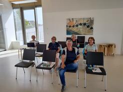 Kooperationspartner Frauke D&uuml;&szlig;mann und vier Seniorinnen sitzen auf St&uuml;hlen und gucken in die Kamera.