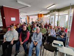 &Uuml;ber drei&szlig;ig Senior:innen sitzen an &uuml;ber f&uuml;nf Stuhlraumen in der Kleinen Markthalle in Stendal und blicken nach vorne.