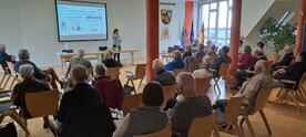 Mobilreferentin Theresa erkl&auml;rt den Begriff Phishing. Die &uuml;ber 20 Teilnehmenden sitzen in dem gr&ouml;&szlig;eren Ratssaal und sind von hinten zu sehen.