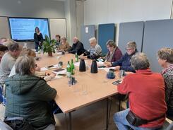 Die Teilnehmenden sitzen zusammen an einem l&auml;ngeren Tisch. Vorne sind Mobilreferentin Theresa und die Titelfolie zum Thema ePA und E-Rezept zu sehen.