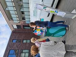 Petra steht mit dem Info-Stand vor dem Info-Mobil am Gl&uuml;cksrad. Drei Seniorinnen stehen um sie herum und eine Seniorin beantwortet eine Frage.