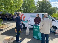 Petra (Mitte) steht an dem Info-Stand des Mobils und ist im Gespr&auml;ch mit einer Frau (links, sie h&auml;lt einen Hund an der Hundeleine) und einem Mann (rechts).