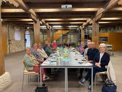 In einem Tagungsraum innerhalb der Burg Dagestein sitzen 16 Personen an einem langen Tisch. Sie blicken in die Kamera. Auf dem langen Tischen liegen Zettel und Brosch&uuml;ren.
