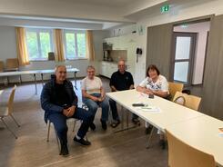 An einem Tischende sitzen zwei M&auml;nner und zwei Frauen, die l&auml;chelnd in die Kamera nach vorne blicken.