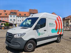 Das Infomobil steht auf einem gepflasterten Platz mit H&auml;usern im Hintergrund.