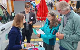 Eine Frau und ein Mann stehen am Infostand; die Frau h&auml;lt einen Flyer in der Hand. 